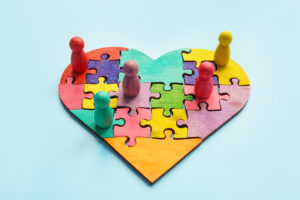 Ilustracja przedstawiająca kolorowe postacie układające puzzle w kształcie serca – symbol budowania relacji, zaufania i lojalności pacjenta w patient experience